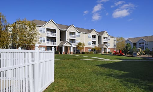 A white picket fence in front of a large apartment building.