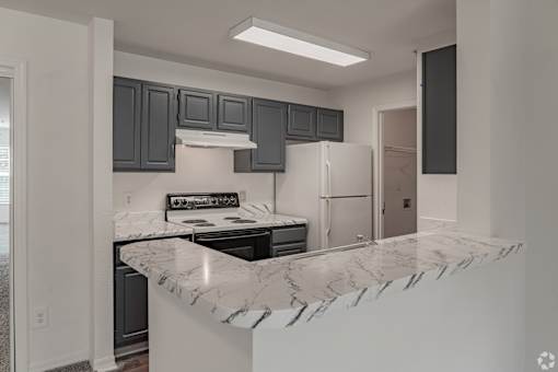A kitchen with a marble countertop and dark grey cabinets.