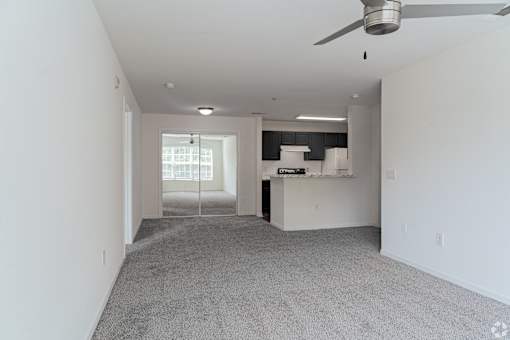 A spacious living room with a ceiling fan and a kitchen area in the background.
