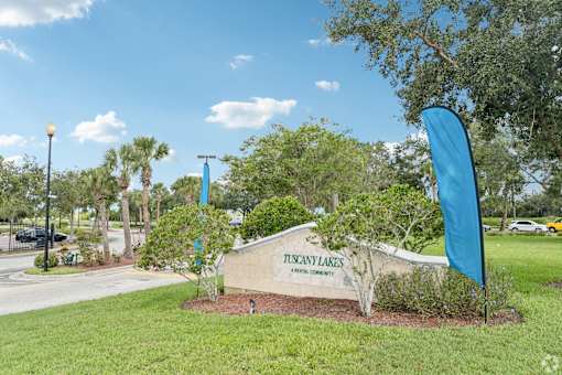 A sign that says Tuscany Lakes is in front of a grassy area.