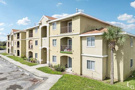 A row of beige apartment buildings with balconies and a palm tree in front.