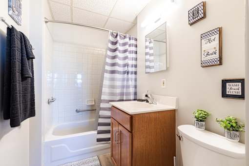 A bathroom with a white tub, a wooden vanity, and striped shower curtain.