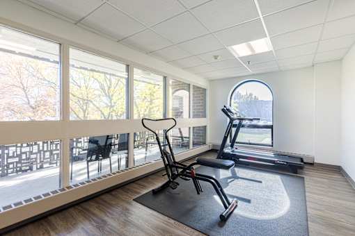 A gym room with a treadmill, exercise bike, and a chair.