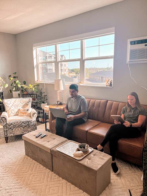 Two people sitting on a couch in a living room with a coffee table in front of them.