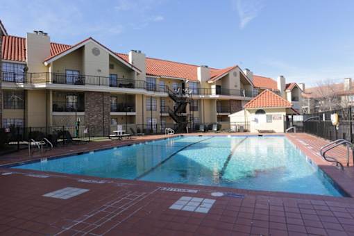A large outdoor swimming pool surrounded by a red tile floor and apartment buildings.