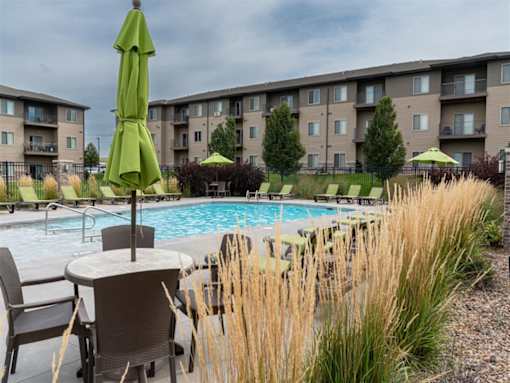 A pool area with chairs and umbrellas in front of apartment buildings.