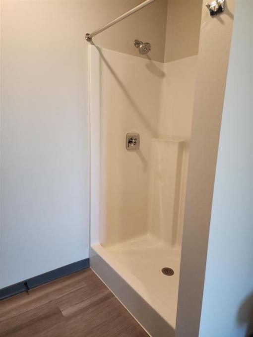 A white shower stall with a door and a drain.