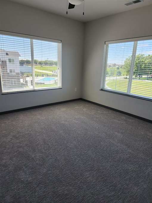 A room with carpeted floor and two windows overlooking a pool and a fence.