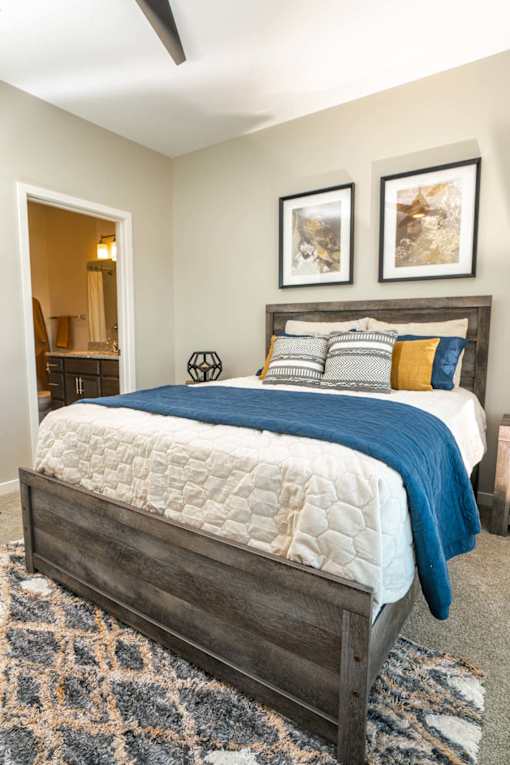 A bed with a blue blanket and pillows is in the foreground of a room.