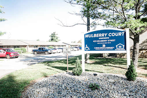 A blue sign for Mulberry Court is in front of a parking lot.