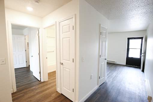 A room with white walls and wooden floors with a door open to another room.