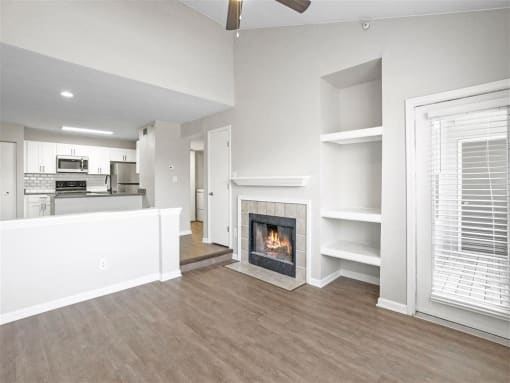 Open-concept living space with vaulted ceilings, a cozy fireplace, built-in shelving, and modern hardwood-style flooring adjacent to the kitchen.