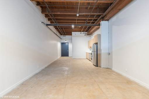 A long, empty hallway with a door at the end and a refrigerator on the side.