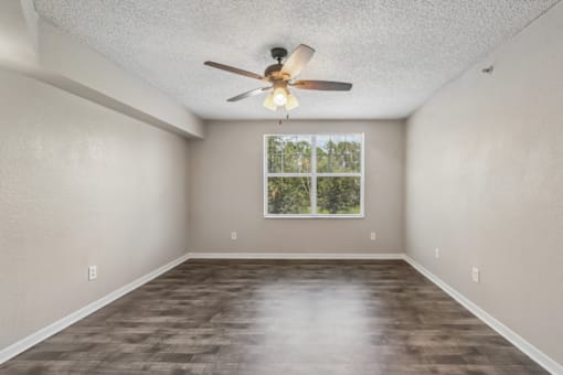 Bright living room with large window, wood-style flooring, and ceiling fan in a 1-bedroom apartment at Gregory Cove in Jacksonville, FL.