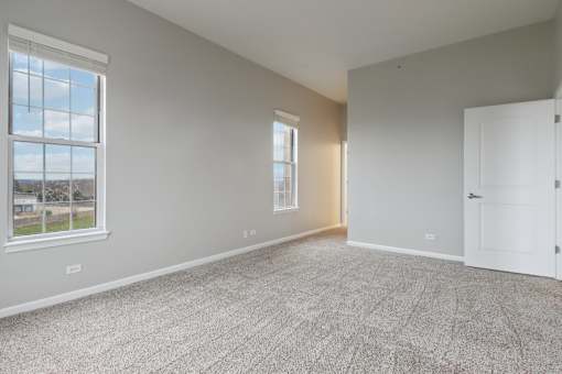 A room with a carpeted floor and two windows.
