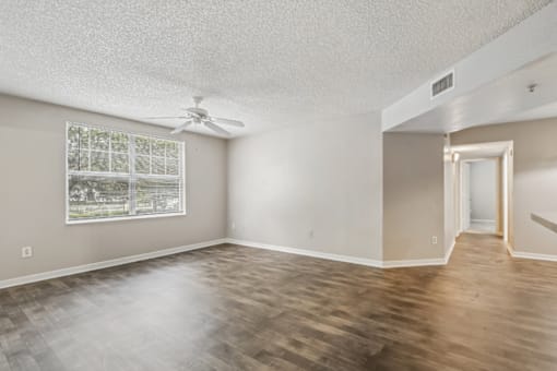 Bright living room with large window, wood-style flooring, and open floor plan in a 3-bedroom, 2-bath apartment at Gregory Cove in Jacksonville, FL.