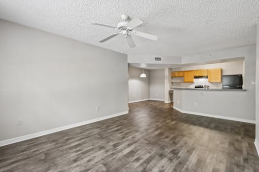 Spacious open-concept living room with wood-style flooring, breakfast bar, ceiling fan, and kitchen in a 3-bedroom, 2-bath apartment at Gregory Cove in Jacksonville, FL.