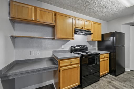 Kitchen with black appliances, wood cabinetry, spacious countertops, and built-in shelving in a 3-bedroom, 2-bath apartment at Gregory Cove in Jacksonville, FL.
