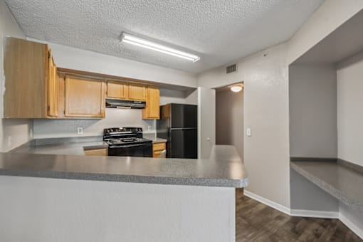 Kitchen with natural wood cabinetry, black appliances, generous counter space, and breakfast bar in a 1-bedroom apartment at Gregory Cove in Jacksonville, FL.