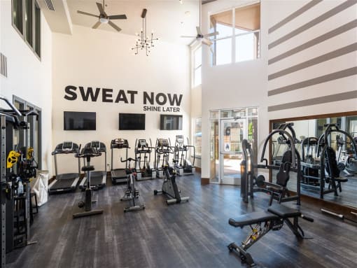 a gym with weights and cardio machines and a sweat now sign on the wall