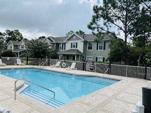 A pool surrounded by a black fence and a building in the background.
