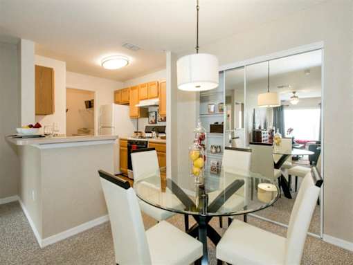 A modern kitchen with a glass dining table and white chairs.