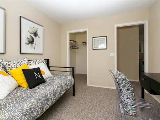 A bedroom with a bed, chair, and two pictures on the wall.