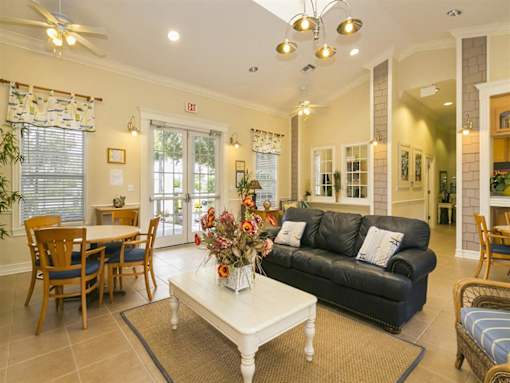 A living room with a black couch, a dining table with chairs, and a coffee table with a vase of flowers.