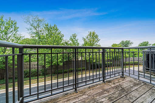 A wooden deck with a metal railing overlooks a road and greenery.