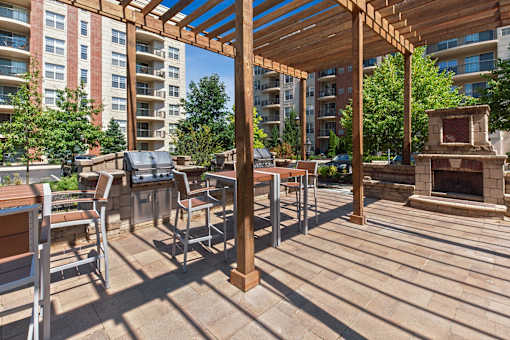 A wooden pergola with a fireplace is in the middle of a patio.