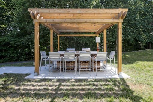 A wooden pergola with a large table and chairs by two BBQ grills at The Crossings at Russett in Laurel, MD