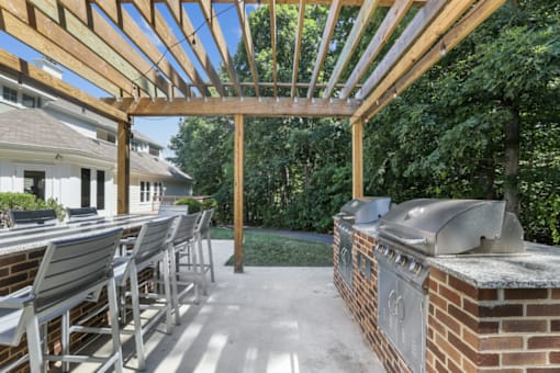 A wooden pergola with a large table and chairs by two BBQ grills at The Crossings at Russett in Laurel, MD