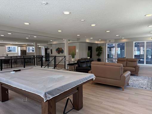 A large room with a mattress on a wooden frame in the foreground and a couch and chairs in the background.