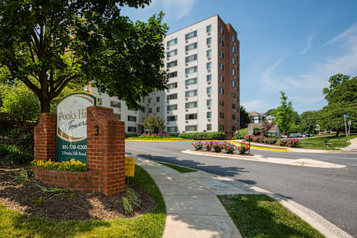 A brick sign for Pooks Hill Towers stands in front of a modern apartment building.