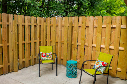 A yellow chair with a floral pillow sits in front of a wooden fence.