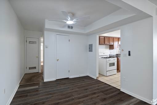 A room with a ceiling fan and a kitchen area in the background.