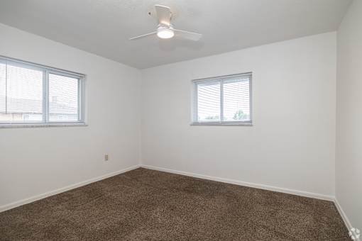 A room with a carpeted floor and two windows.