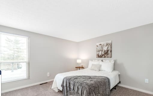 A bedroom with a bed, lamp, and painting on the wall.