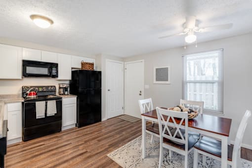 A kitchen with a black fridge and microwave, a wooden dining table with chairs, and a rug on the floor.