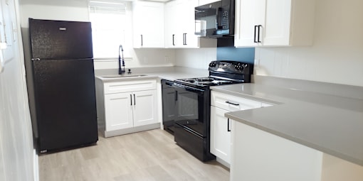 an empty kitchen with white cabinets and a black refrigerator