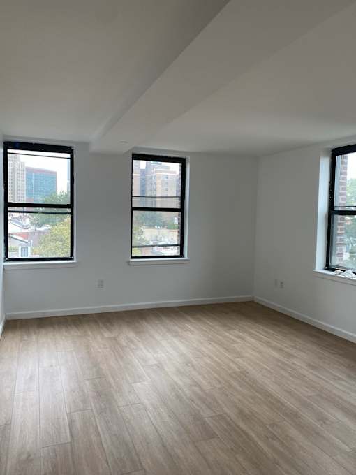 A room with wooden flooring and three windows.