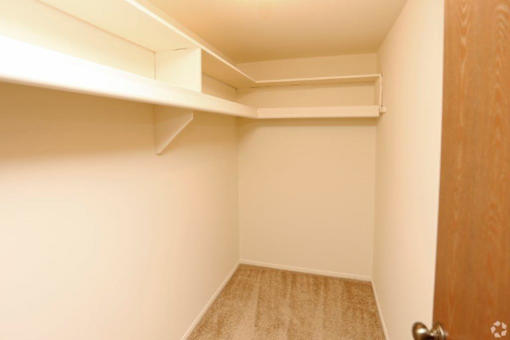 a walk in closet with a wooden door and white walls