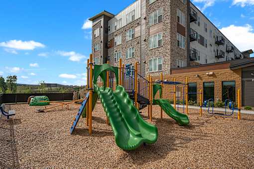 A playground with a green slide and a building in the background.