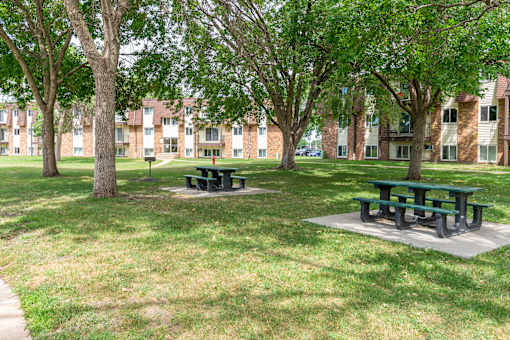 two picnic tables in a grassy area in front of a brick building