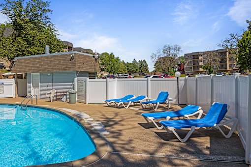 a swimming pool with blue chaise lounge chairs and a poolside building with apartments at Heritage Hills Apartments, Bloomington Minnesota