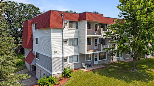 a white and red apartment building with a yard and trees at Heritage Hills Apartments, Minnesota