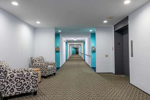 a long hallway with white and blue walls and a carpeted floor and some chairs at Humboldt Senior 55+ Apartments, Saint Paul, 55107
