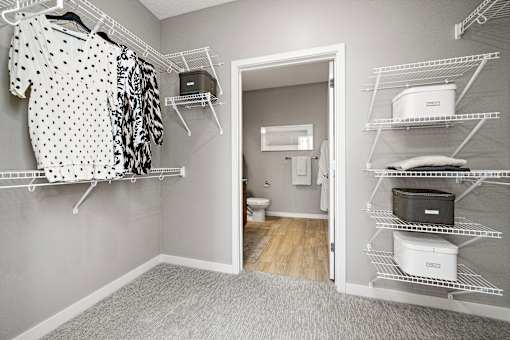 A walk in closet with clothes hanging and shelves with storage boxes.