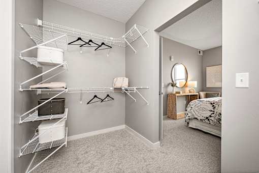 A bedroom with a bed, a mirror, and a closet with clothes hanging.