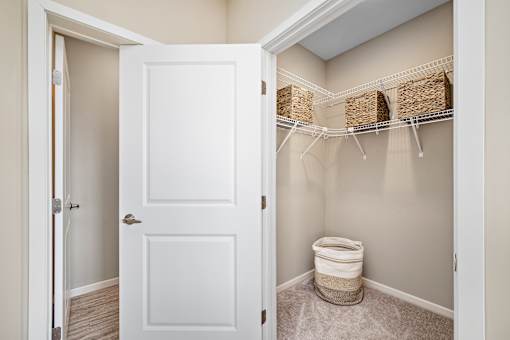 A white door is open to a bathroom with a toilet and storage baskets at The Winslow 62+ Apartments, Minnesota